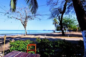 Vista a la playa con mesa y silla de madera, palmeras y una vista despejada del océano.