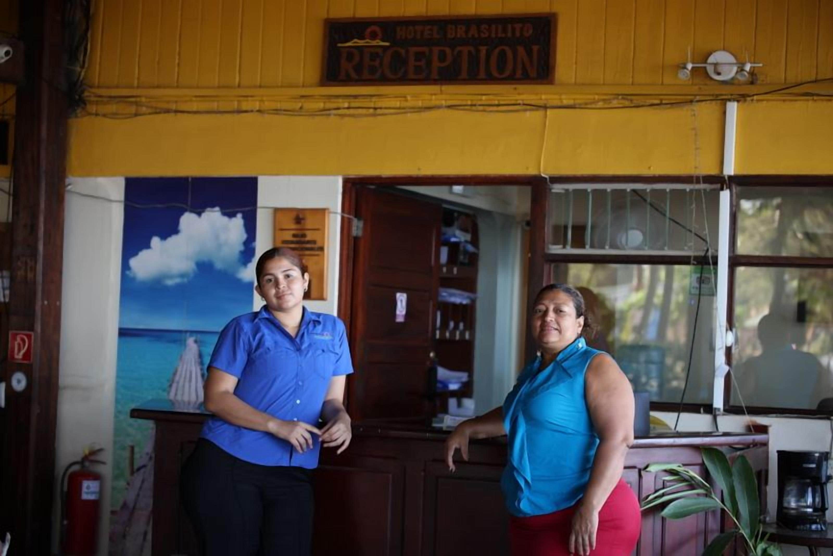 A reception area with a sign reading "Hotel Brasilito Reception," a wooden counter, and a painting of a sailboat on the wall.