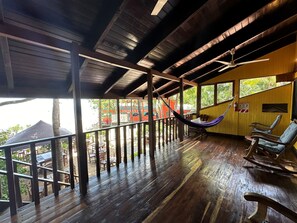 Ένα ξύλινο κατάστρωμα με μια αιώρα και πολυθρόνες, με θέα σε έναν δρόμο όπου είναι παρκαρισμένα αυτοκίνητα και βρίσκονται κτίρια.