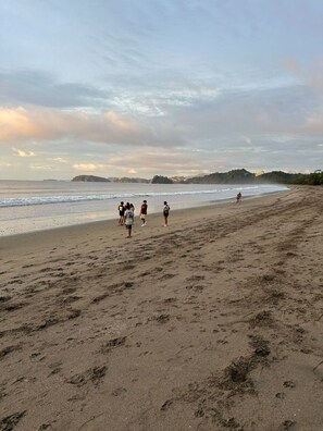 A beach with footprints, a group of people, and a distant shoreline. - Hotel Brasilito (Cabo Velas)