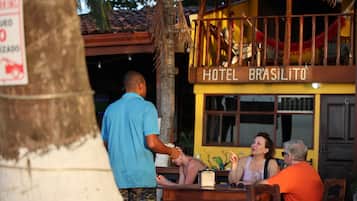 A hotel named 'HOTEL BRASILITO' with a signboard, a palm tree, and a wooden table with people seated.