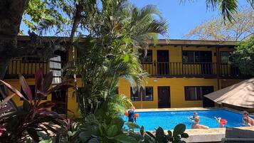 A pool area with a yellow building, palm trees, and a clear blue sky.