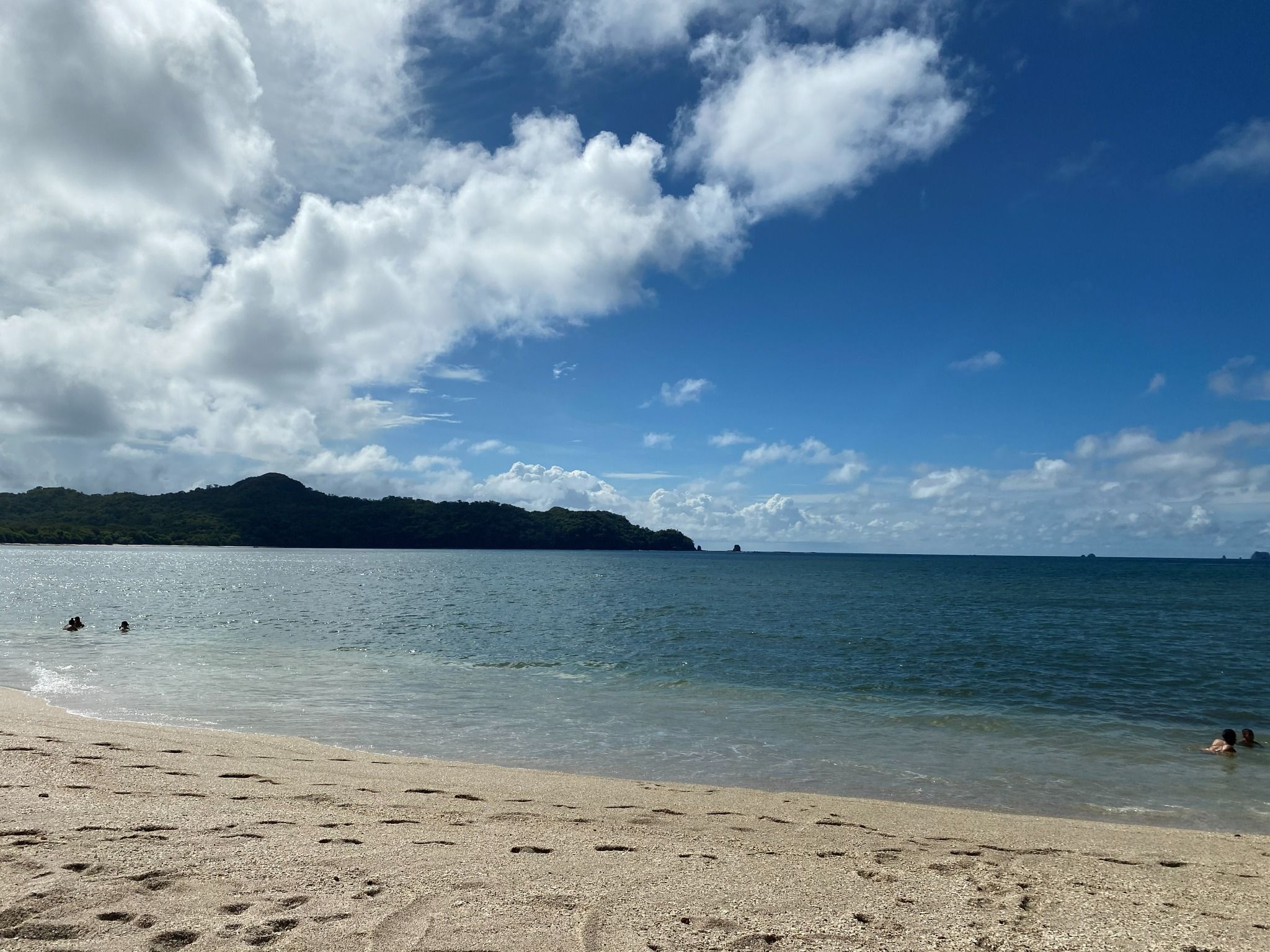 A beach with clear water, a sandy shore, and a distant mountain.