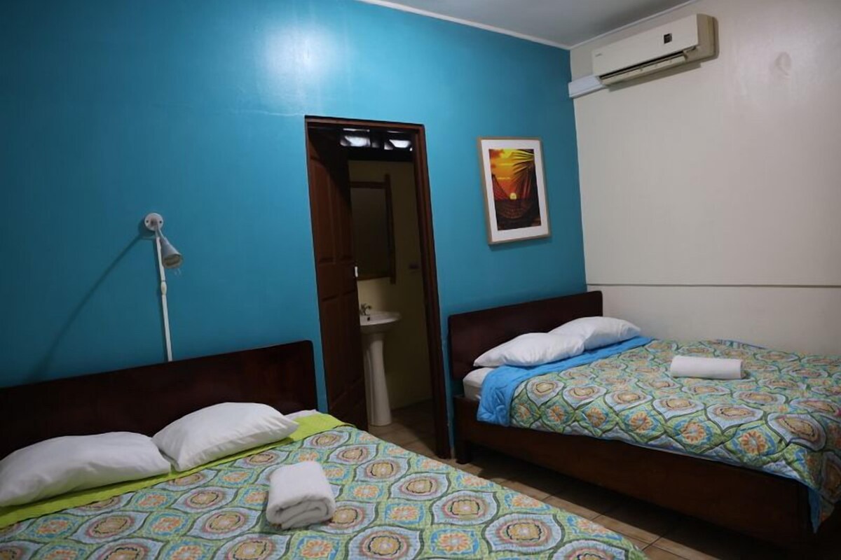 A room with two beds, a door leading to a bathroom, and an air conditioning unit on the wall.