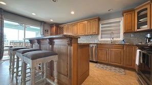 A kitchen with wooden cabinets, a stainless steel dishwasher, and a bar area with stools.