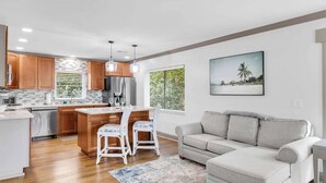 A modern kitchen with wooden cabinets, a stainless steel refrigerator, and a dining area with two white chairs.