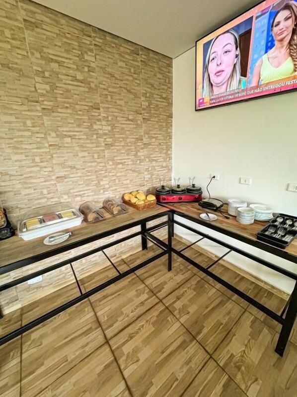 Ein modernes Wohnzimmer mit Holzboden, einem großen, an der Wand befestigten Fernseher und einem Esstisch mit verschiedenen Speisen und Besteck.