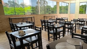 Un comedor con varias mesas y sillas, amplias ventanas que ofrecen vistas a zonas verdes y edificios.