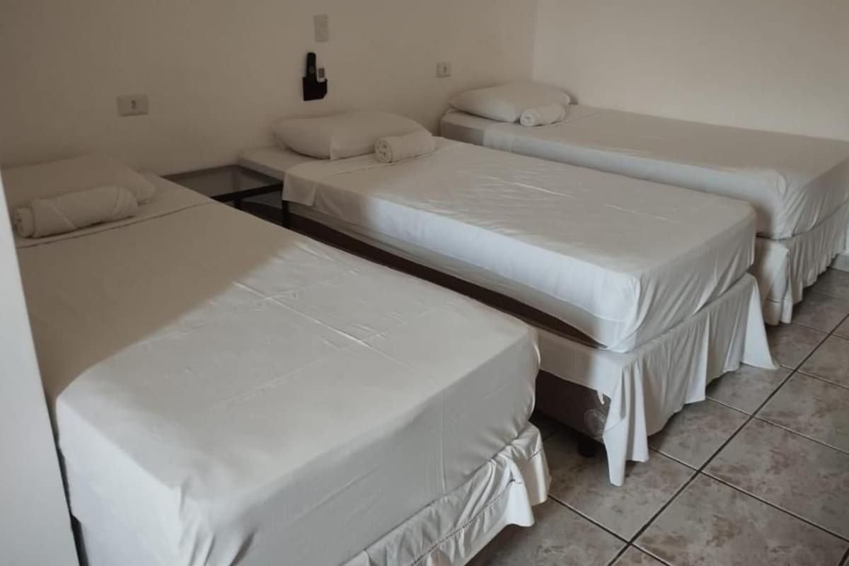 Ein Zimmer mit drei Einzelbetten, jedes mit einer weißen Matratze und einem Kissen.