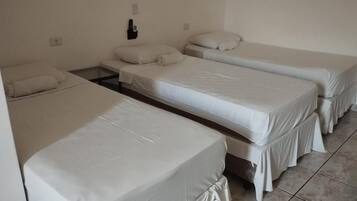 Quarto com três camas de solteiro, cada uma com colchão e travesseiro brancos.
