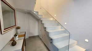 Moderni portaikko, jossa on lasikaiteet ja valkoiset portaat, ja joka johtaa ylempään kerrokseen.