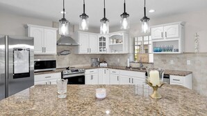 Una cocina moderna con encimeras de granito, electrodomésticos de acero inoxidable e iluminación colgante.