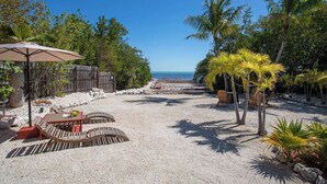 A beachside patio with a table and chairs, a wooden fence, and palm trees. - Seaside Dream House 3bed/2bath single family with open water views (Marathon)