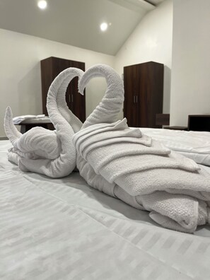 A neatly folded white towel arranged in a swan shape on a bed in a modern hotel room with wooden wardrobes and a white ceiling. - The Glen Yard Farms (Mohadi)