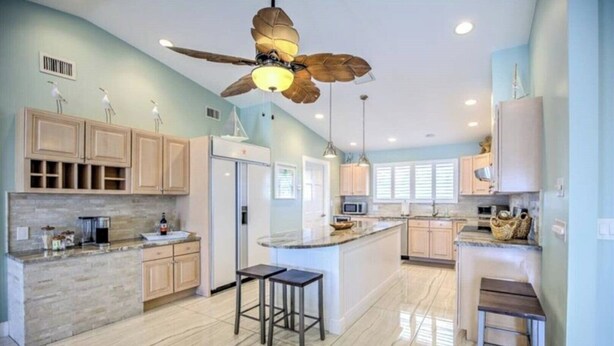 A spacious kitchen with a central island, wooden cabinets, a ceiling fan, and a large window. - Splash Into Me! New 3 BR in Key Colony w/ dockage + private pool (KEY COLONY BEACH)