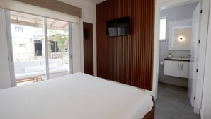 Un dormitorio moderno con una cama grande, un televisor montado en una pared de paneles de madera y una puerta corrediza de vidrio que da a un balcón.