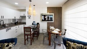 Una cocina moderna con armarios blancos, un comedor con mesa y sillas de madera, y un sofá azul con cojines estampados.