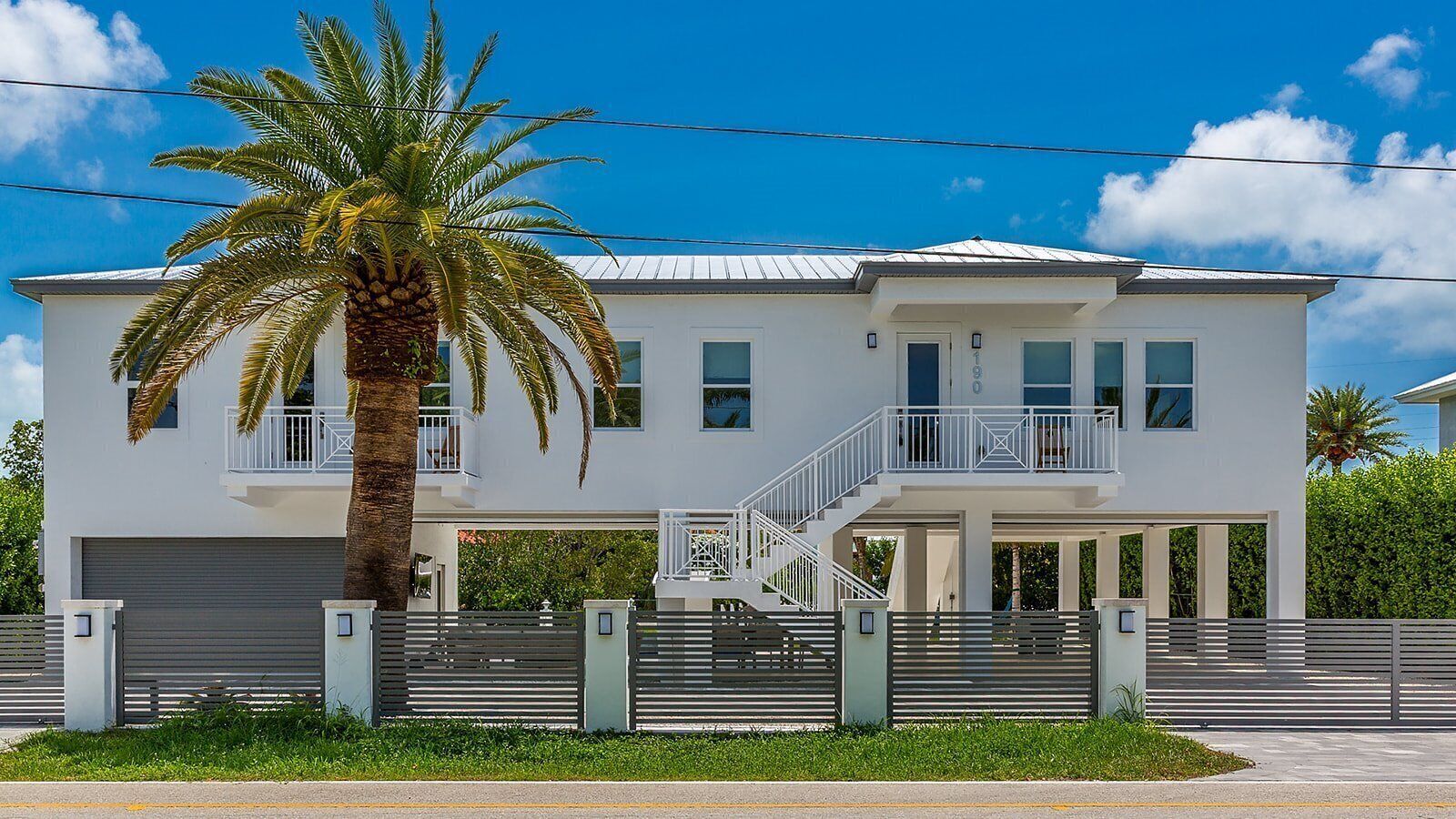 A two-story house with a covered porch, a palm tree, and a gated driveway.