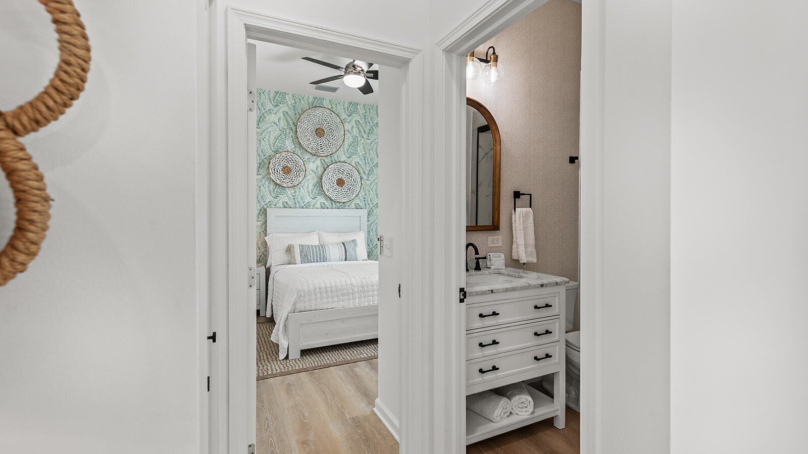 Un dormitorio con cama, tocador con cajones, ventilador de techo y pared con espejo y perchero.
