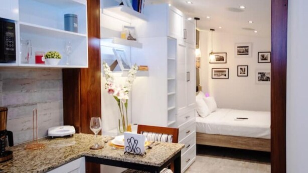 A compact, modern room with a kitchen area, a dining table, and a bed.