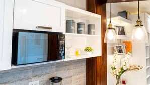 A modern kitchen with white cabinetry, a built-in microwave, and a coffee machine.
