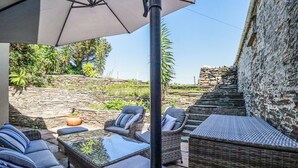 Un espace extérieur aménagé avec des meubles en osier et une table à plateau de verre, un mur en pierre et une vue sur un paysage naturel.