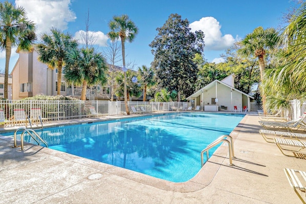 A swimming pool with a white fence, lounge chairs, and palm trees.