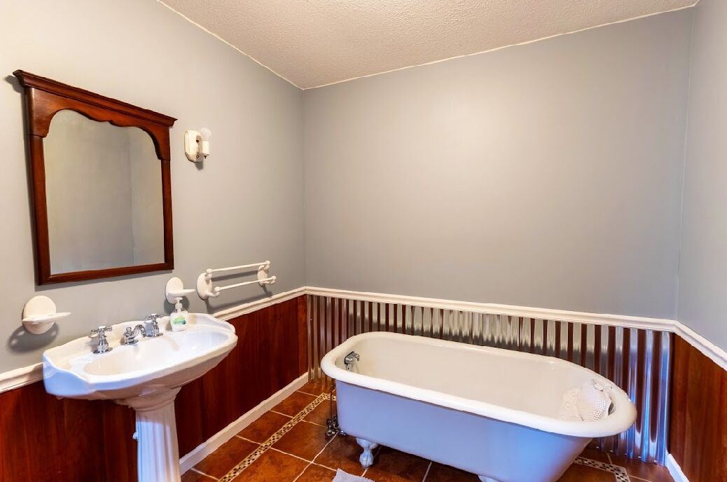 Une salle de bain avec une baignoire sur pieds, un lavabo sur colonne et un grand miroir.