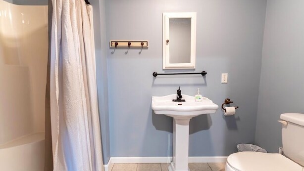 Un baño con lavamanos pedestal blanco, inodoro, toallero y cortina de ducha.