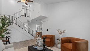 A modern living room with a staircase, a coffee table with books and a decorative piece, two brown armchairs, and a potted plant. - Multi Home - Up to 16 people - Balcony Access (Austin)