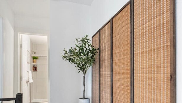 A hallway with a wooden floor, a black side table with a potted plant, and a room visible through an open door. - Multi Home - Up to 16 people - Balcony Access (Austin)