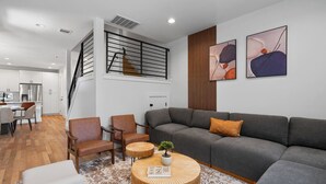 A modern living room with a grey sofa, two armchairs, a coffee table, and a staircase leading to a kitchen.