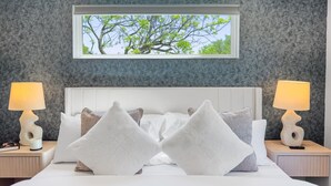 A modern hotel room with a large bed, two bedside tables with lamps, and a window with a view of trees.