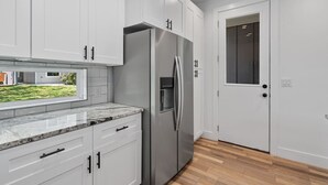 A modern kitchen with white cabinets, a stainless steel refrigerator, and a wooden floor.