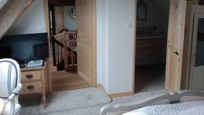 A bedroom with a sloped ceiling, wooden beams, a bed, a desk with a chair, and a television. - Le Presbytere (Beauficel)