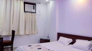 Quarto com cama, cadeira, mesa de cabeceira, ventilador de teto e janela com cortinas.