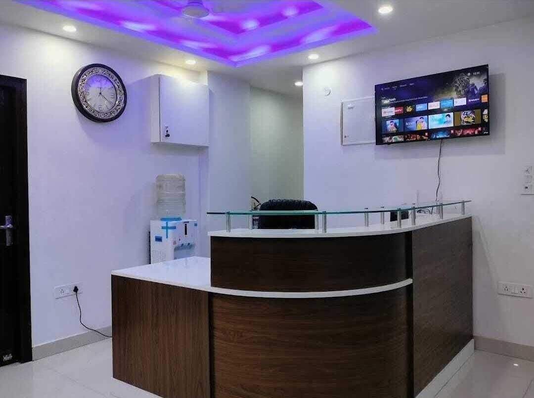 Un área de recepción con un mostrador de madera, un televisor empotrado que muestra varios canales y un reloj en la pared.