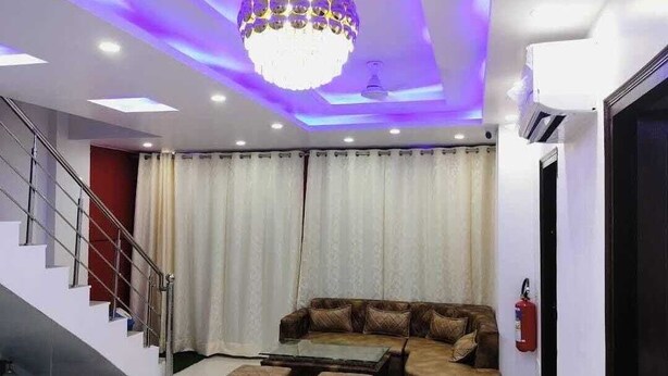 Uma sala de estar moderna com um sofá seccional, pufes, uma mesa de centro de vidro, um candelabro e uma escada.