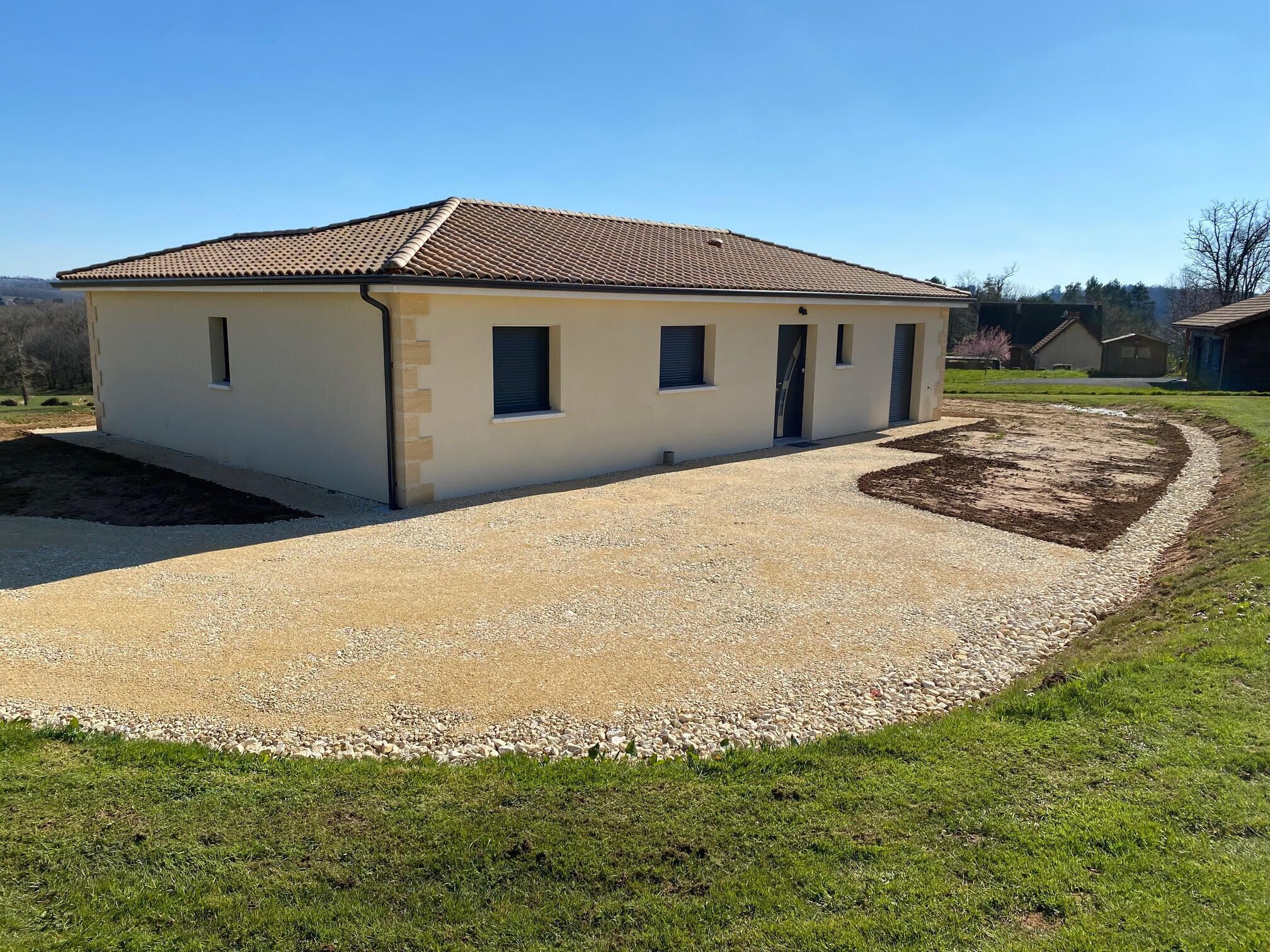 A single-story building with a tiled roof, a gravel driveway, and a landscaped garden area.
