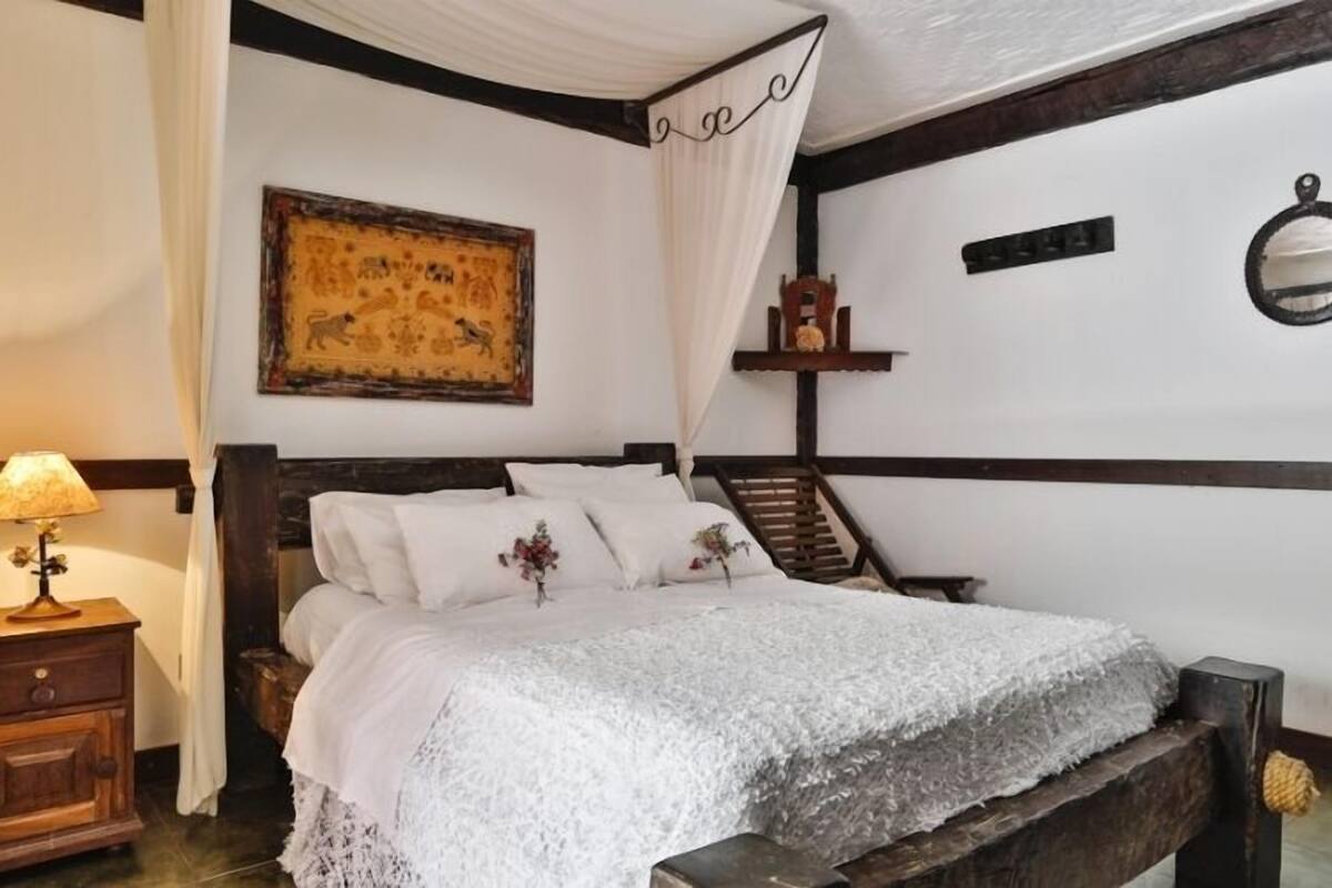 A bedroom with a bed, a nightstand, a wooden headboard, a wall-mounted shelf, and a staircase.