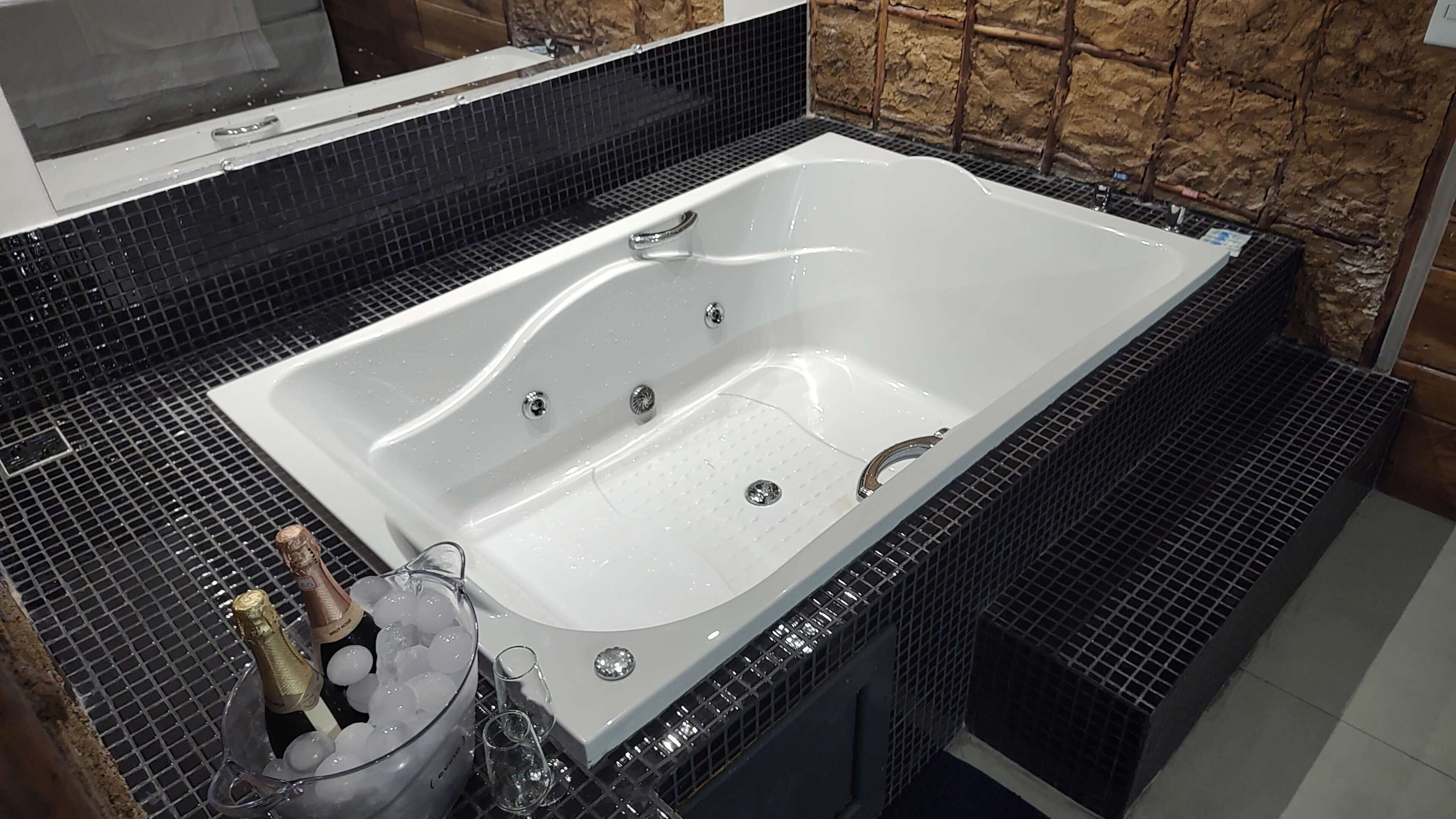 A modern bathroom with a large white bathtub, black tiled walls, and a stone accent wall.