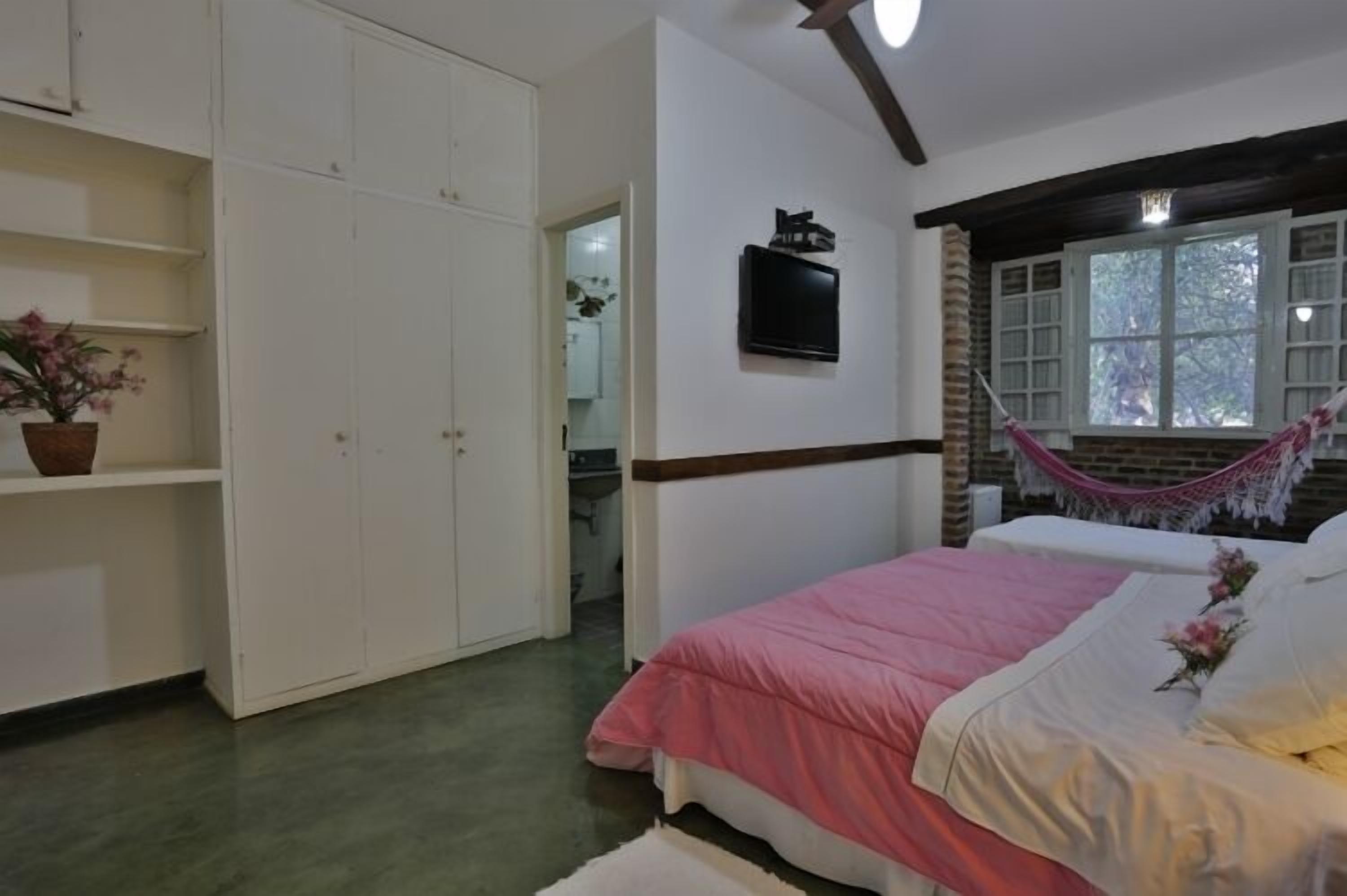 Een slaapkamer met een bed, een kledingkast, een televisie en een hangstoel.