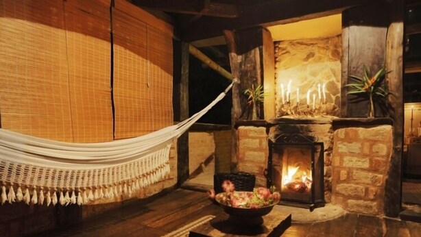 A cozy room with a fireplace, a hammock, and a bowl of fruit on a table.