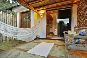 Un espacio al aire libre techado con una hamaca, un banco de madera y un tapete blanco sobre un suelo de baldosas.