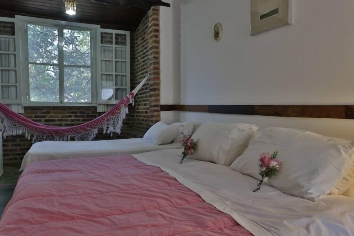 A bedroom with two beds, a hammock, and a window with a view of trees.