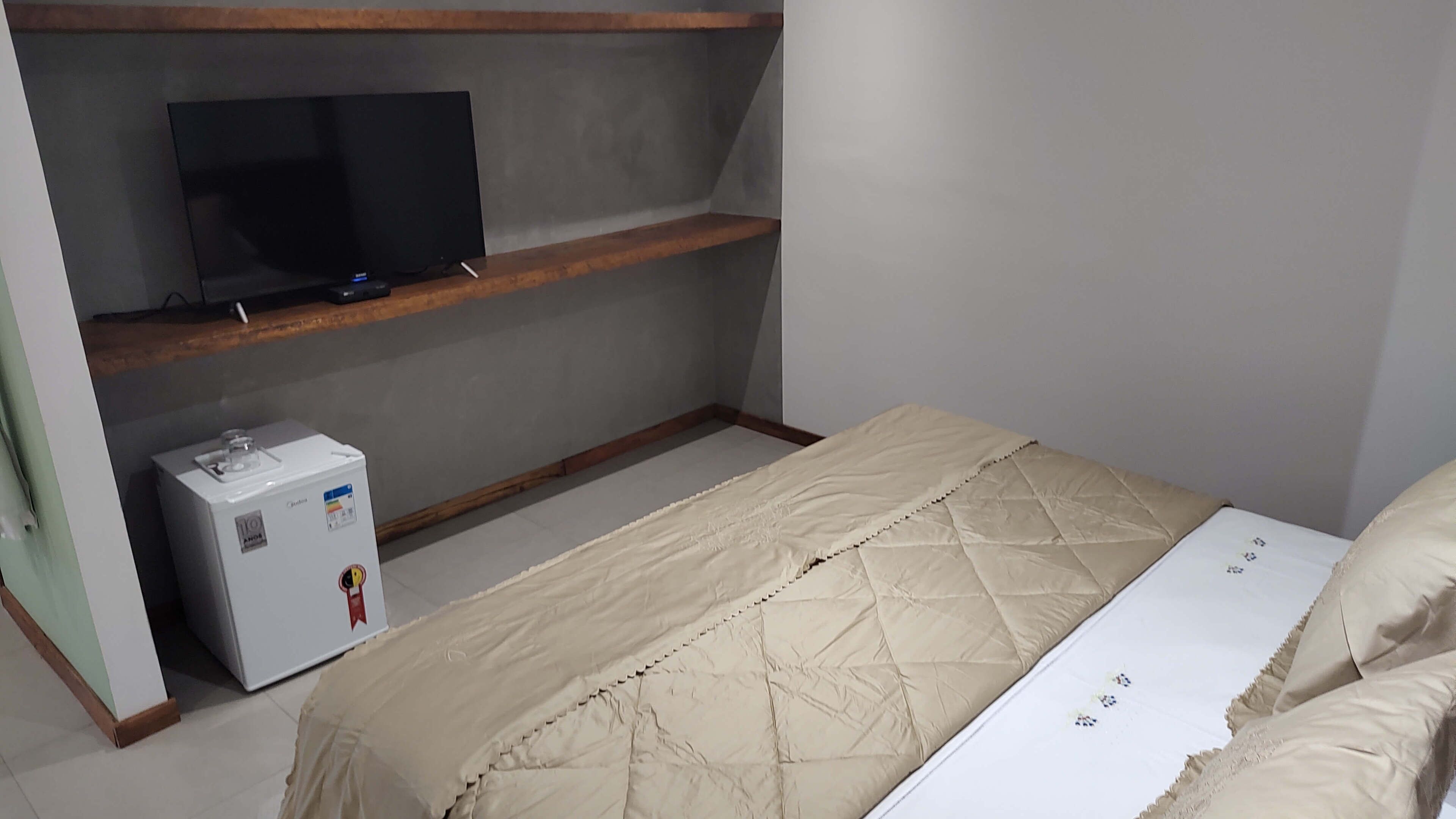 Une chambre à coucher avec un lit, un téléviseur posé sur une étagère et un petit appareil électroménager sur le sol.