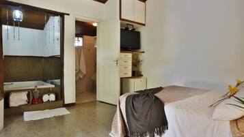 A bedroom with a bed, a television on a stand, a wardrobe, and a bathroom with a bathtub and towel rack.