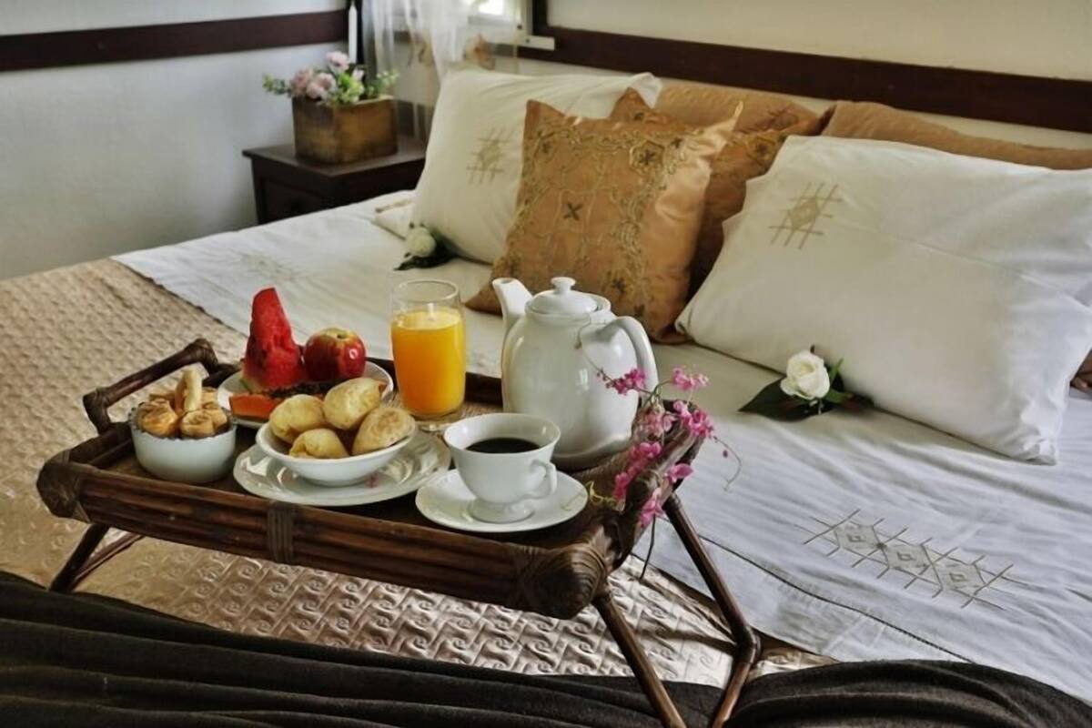 A neatly made breakfast tray with pastries, fruits, and beverages on a bed with a white bedspread and decorative pillows.