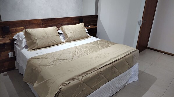 A neatly made bed with a beige quilt and pillows, a wooden headboard, and a bedside table with a lamp. - Pousada Solar Dos Ipês (Santana do Riacho)
