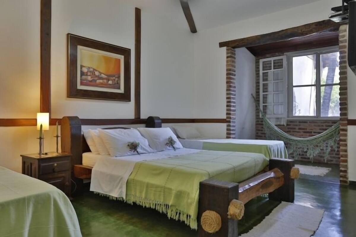 A bedroom with two beds, a hammock, a framed picture on the wall, and a window with a view of the outdoors.